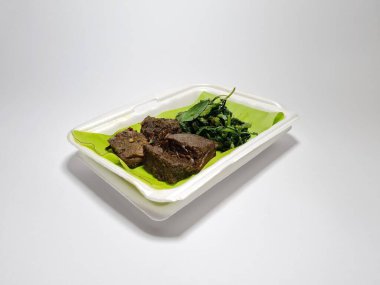 Beyaz kabın içinde yeşil sebzeli kızarmış et dilimleri.