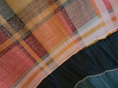 Soyut arkaplan desenli kumaş, turuncu, ekose, yeşil, siyah ve beyaz çizgilerle birleştirilmiş.