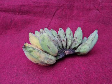 Kırmızı zemin üzerinde yarı olgun, yeşil, sarı muzlar.