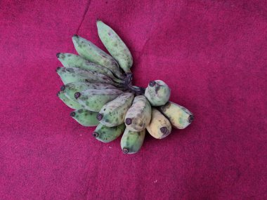 Kırmızı zemin üzerinde yarı olgun, yeşil, sarı muzlar.