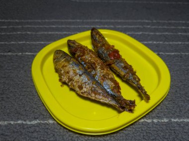 Sarı bir kabın içinde tatlı ve ekşi tatla pişirilmiş üç deniz balığı.
