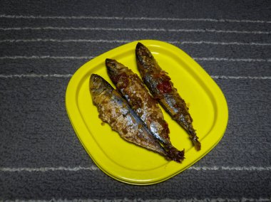 Sarı bir kabın içinde tatlı ve ekşi tatla pişirilmiş üç deniz balığı.