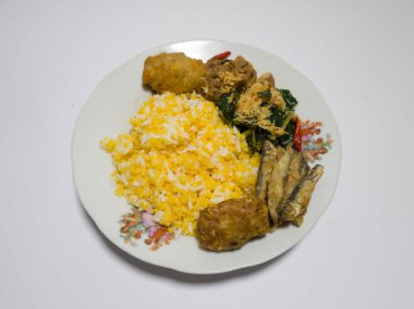 Mısır pilavı, kızarmış balık, yeşil sebzeler rendelenmiş hindistan cevizi serpiştirilmiş, tuzlu bir tabakta servis edilmiş.