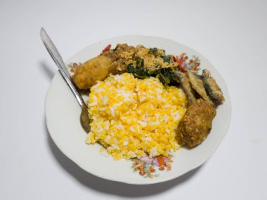 Mısır pilavı, kızarmış balık, yeşil sebzeler rendelenmiş hindistan cevizi serpiştirilmiş, tuzlu bir tabakta servis edilmiş.