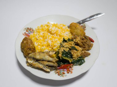 Mısır pilavı, kızarmış balık, yeşil sebzeler rendelenmiş hindistan cevizi serpiştirilmiş, tuzlu bir tabakta servis edilmiş.