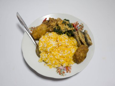 Mısır pilavı, kızarmış balık, yeşil sebzeler rendelenmiş hindistan cevizi serpiştirilmiş, tuzlu bir tabakta servis edilmiş.