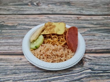 Kızarmış erişteli pilav, kızarmış yumurta, sosis dilimleri ve salatalık dilimleri.