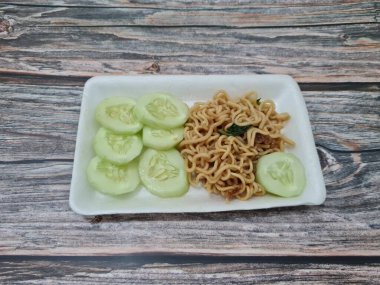 Beyaz bir kabın içinde salatalık dilimli kızarmış erişte.