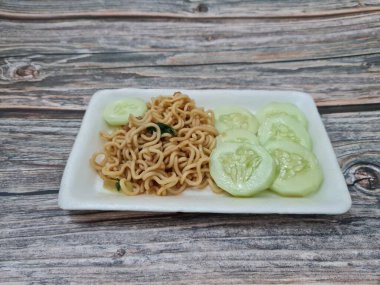 Beyaz bir kabın içinde salatalık dilimli kızarmış erişte.