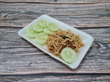 Beyaz bir kabın içinde salatalık dilimli kızarmış erişte.