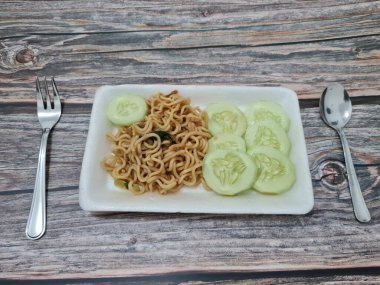 Beyaz bir kabın içinde salatalık dilimli kızarmış erişte.