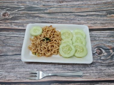 Beyaz bir kabın içinde salatalık dilimli kızarmış erişte.