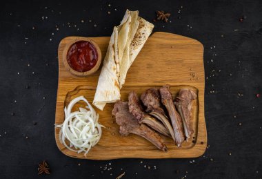 Kemiğin üstünde kızarmış kebap, sosla ve tahtanın üzerinde siyah bir zemin üzerinde ekmek.