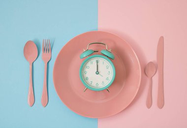 Pembe plaka üzerinde açık mavi alarm saati fikri, fitne ve diyet fikriyle pop sanatının arka planına sahip klasik bir renk. Zamanında ye ve akıllı ol.