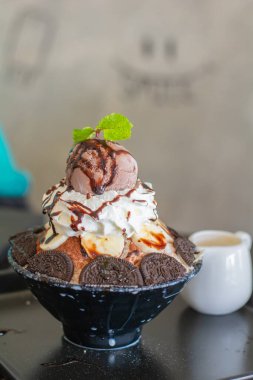 Çikolatalı dondurma, krem şanti, muz dilimi, bingsu 'nun üstüne siyah kâse, kafeteryada ve restoranda ahşap masa. Lezzetli Kore buzlu dondurması.