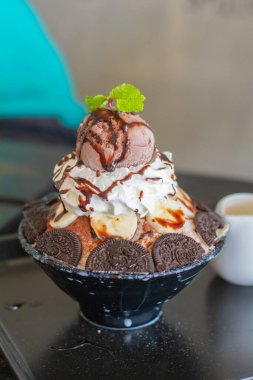 Çikolatalı dondurma, krem şanti, muz dilimi, bingsu 'nun üstüne siyah kâse, kafeteryada ve restoranda ahşap masa. Lezzetli Kore buzlu dondurması.