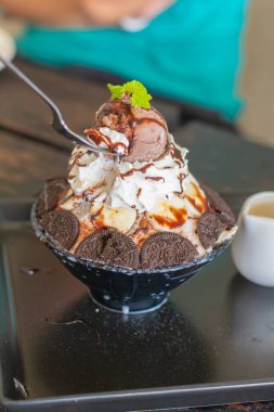 Çikolatalı dondurma yemek, krem şanti, muz dilimi, bingsu 'nun üstünde siyah kâse, kafeteryada ve restoranda ahşap masa. Lezzetli Kore buzlu dondurması.
