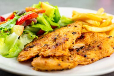 Ev yapımı yemek konsepti. Beyaz bir tabakta salata ve patates kızartmasıyla servis edilen karabiberli tavuk göğsü bifteği. Yüksek protein gıdası.