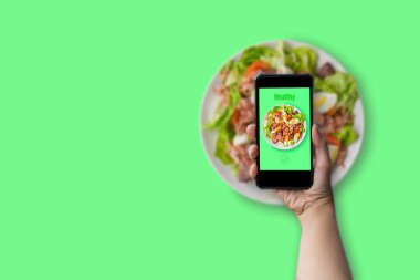 Sağlıklı gıda konsepti. Ton balığı salatası, haşlanmış yumurta, marul ve domatesli yeşil tabakta yeşil arka planda sağlıklı yeşil metinli akıllı telefon.. 
