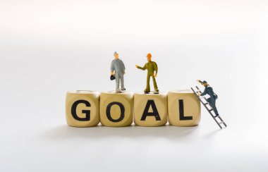 Minyatür insanlar, küçük model insan figürü ayakta duruyor ve tahta kelime kutusuna (gol) tırmanıyor. Konseptte iş başarısı. Metnin için boşluk kopyala.