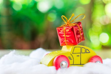 Sarı ahşap arabanın çatısındaki kırmızı hediye kutusu beyaz pamuğun üzerinde yeşil bokeh arkaplanlı, metin için boşluk kopyala. Noel ve yeni yıl konsepti.
