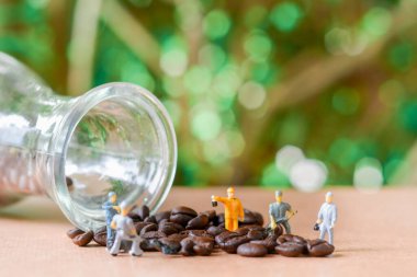 Takım çalışması yapan bir grup minyatür insan, küçük model insan figürü yeşil bokeh arka planlı ahşap masadaki kahve çekirdeklerini temizliyor. Uzayı kopyala Yiyecek ve içecek konsepti.