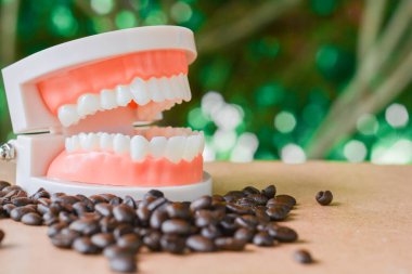 Takma diş ve kahve çekirdeği ahşap masada. Uzayı kopyala Diş konsepti için sağlıksız içecek.