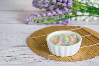 Hindistancevizi sütünde (Bua Loy) pirinç hamuru ahşap masada mor çiçekli beyaz kasede. Lezzetli Tayland tatlıları.