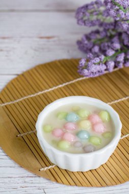 Hindistancevizi sütünde (Bua Loy) pirinç hamuru ahşap masada mor çiçekli beyaz kasede. Lezzetli Tayland tatlıları.