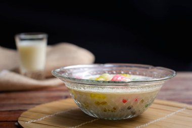 Renkli pirinç gnocchi taze hindistan cevizi sütlü cam kasede kahverengi masa örtüsünde siyah zeminde. Lezzetli Tayland tatlıları.