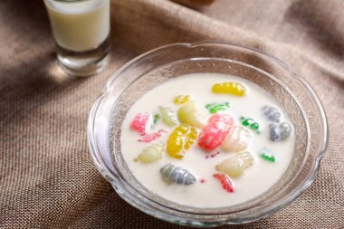 Renkli pirinç gnocchi taze hindistan cevizi sütlü cam kasede kahverengi masa örtüsünde siyah zeminde. Lezzetli Tayland tatlıları.