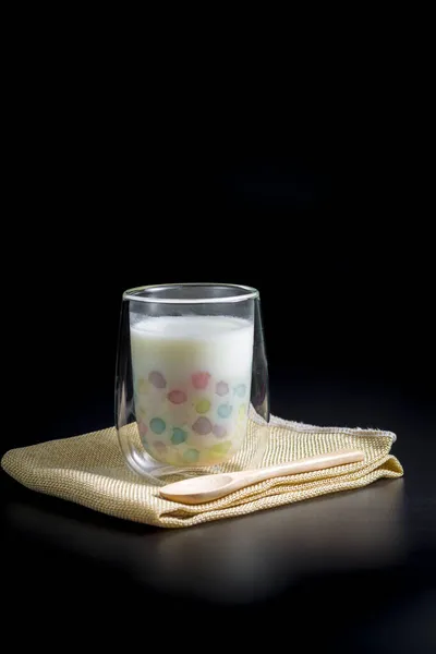 Color rice dumpling in coconut milk (Bua Loy) in transparent glass on brown table cloths on black background. Delicious Thai dessert.