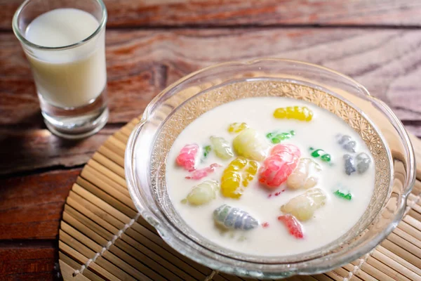 Renkli pirinç gnocchi taze hindistan cevizi sütlü cam kasede kahverengi masa örtüsünde siyah zeminde. Lezzetli Tayland tatlıları.