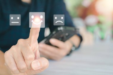 Müşteri memnuniyeti değerlendirmesi ve konsept. Müşteriler ya da iş adamları başvurudaki hizmetleri değerlendirmek için cep telefonu kullanırlar ve puan ve işaret eden gülümseme yüzleri gösterirler.