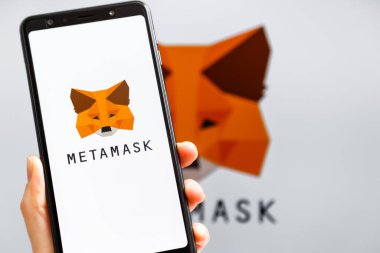 Ukrayna, Odessa - 9 Ekim 2021: MetaMaske uygulaması arka planda MetaMask logosuyla akıllı telefon ekranında çalışan el ele tutuşma uygulaması. MetaMaske yazılım şifreleme cüzdanıdır.