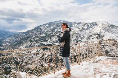 Vouraikos geçidinde dağın tepesindeki gözlem güvertesinde duran genç bir kadın. Karla kaplı muhteşem dağ manzaralı Mega Spileon Manastırı terası. Kış tatili Yunanistan.