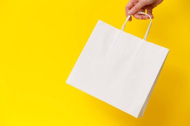 Sarı arka planda beyaz boş bir alışveriş çantası tutan kadın. Kara Cuma indirimi, geri dönüşüm, alışveriş ve ekoloji konsepti.