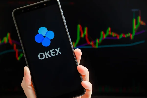 Ukraina, Odessa - oktober, 9 2021: OKEx mobilapp kjører på smarttelefon skjerm med handletabell i bakgrunnen. OKEx er kryptovalutaveksling og handelsplattform. – stockfoto
