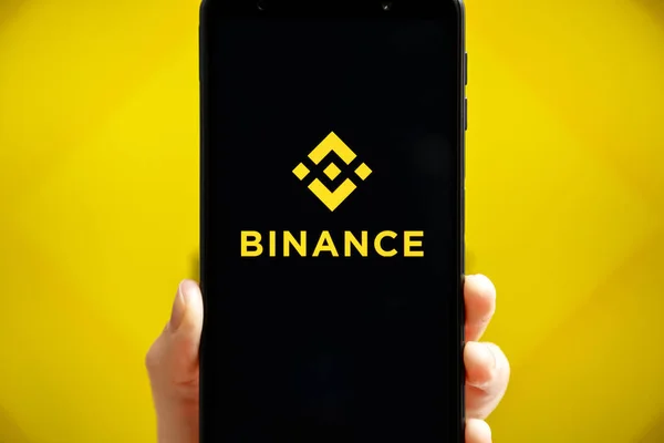 Ukraine, Odessa - 9. Oktober 2021: Handheld-Handy mit Binance-App am Smartphone-Bildschirm mit Binance-Logo im Hintergrund. Binance ist Kryptowährungsbörse und Handelsplattform. — Stockfoto