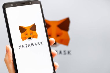 Ukrayna, Odessa - 9 Ekim 2021: MetaMaske uygulaması arka planda MetaMask logosuyla akıllı telefon ekranında çalışan el ele tutuşma uygulaması. MetaMaske yazılım şifreleme cüzdanıdır