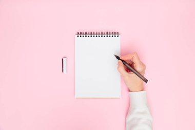 Beyaz, boş, sarmal bir not defteriyle, pastel pembe arka planda izole edilmiş bir kalem ile kadın el yazısı. Düz konum, kopyalama alanı. Yaratıcı çalışma, iş, finans veya eğitim kavramı