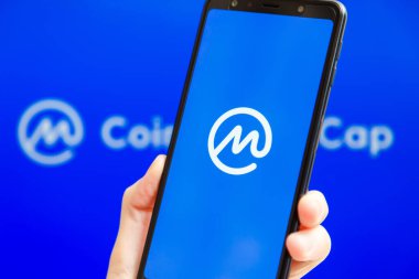 Ukrayna, Odessa - 9 Ekim 2021: Arkaplanda CMC logosu olan akıllı telefon ekranında çalışan CoinMarketCap uygulaması ile el ele tutuşmak. Dünyanın en güvenilir kripto para birimi veri yetkilisi.