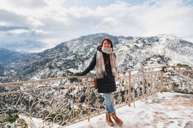 Vouraikos geçidinde dağın tepesindeki gözlem güvertesinde duran genç bir kadın. Karla kaplı muhteşem dağ manzaralı Mega Spileon Manastırı terası. Kış tatili Yunanistan