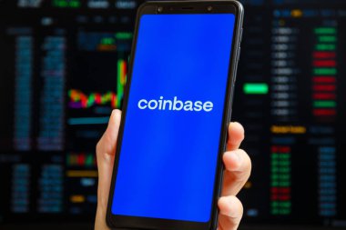 Ukrayna, Odessa - 9 Ekim 2021: Arkaplanda ticaret sayfası olan akıllı telefon ekranında çalışan Coinbase uygulaması ile el ele tutuşma cep telefonu. Para tabanlı Amerikan kripto döviz ve ticaret platformu