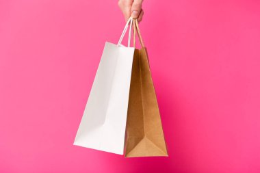 Pembe arka planda iki alışveriş çantası tutan kadın. Beyaz ve kahverengi el işi boş kağıt torbaları. Kara Cuma indirimi, indirim, alışveriş ve ekoloji konsepti