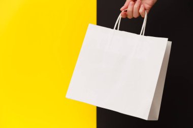 Sarı ve siyah arka planda beyaz boş bir alışveriş çantası tutan kadın. Kara Cuma indirimi, geri dönüşüm, alışveriş ve ekoloji konsepti