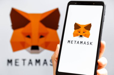 Ukrayna, Odessa - 9 Ekim 2021: MetaMaske uygulaması arka planda MetaMask logosuyla akıllı telefon ekranında çalışan el ele tutuşma uygulaması. MetaMaske yazılım şifreleme cüzdanıdır