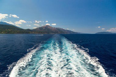 Yaz zamanı bir yolcu gemisinin arkasında açık deniz suyu izi. Feribot, Akdeniz 'in mavi ve berrak sularında Sefalonya Adası, Yunanistan' dan ayrılan bir iz bırakıyor.