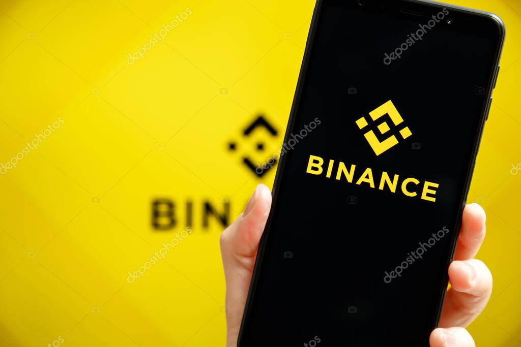Ukraine, Odessa - October, 9 2021: Hand holding mobile with Binance app running at smartphone screen with Binance logo at background. Binance is cryptocurrency exchange and trading platform