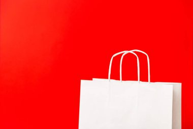 Kırmızı arkaplanda boş beyaz kağıt poşet var. Kara Cuma, indirim, geri dönüşüm, alışveriş ve ekoloji konsepti